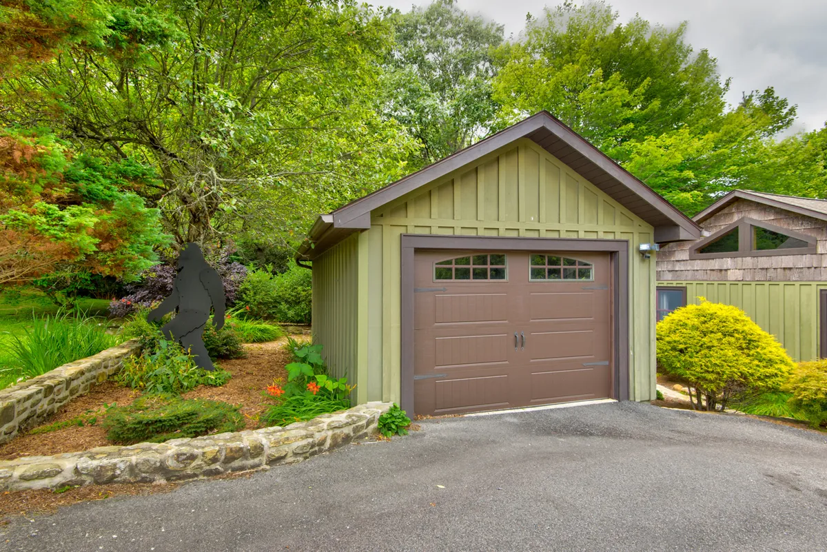 This image shows the exterior of the Bigfoot Bungalow with a focus on the garage door, a unique garden sculpture, and welcoming landscaping. The well-maintained outdoor area is inviting and suggests a peaceful, private setting.