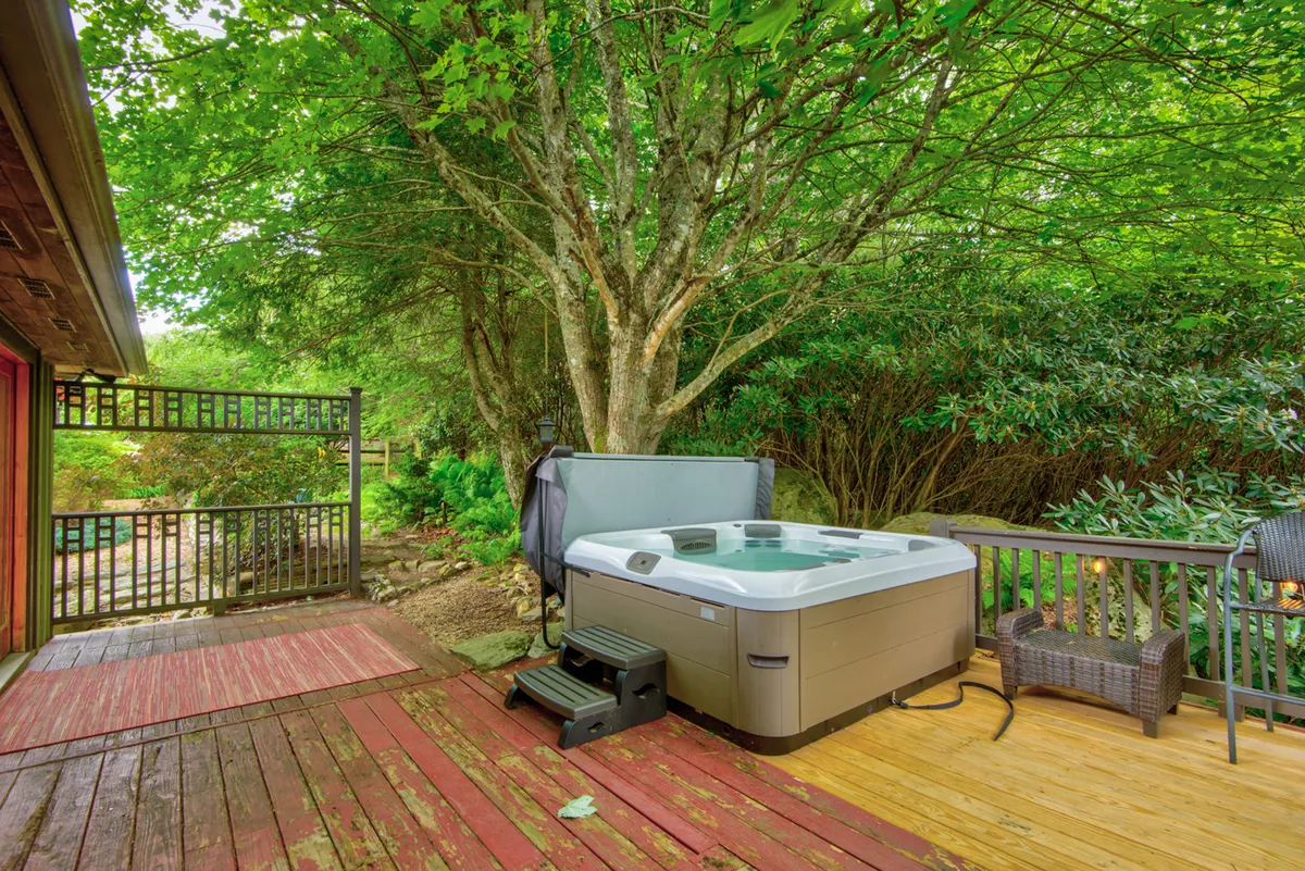 This image features a serene outdoor deck surrounded by lush greenery, with a private hot tub as the focal point. A lounge chair sits nearby, inviting guests to relax and enjoy the tranquil mountain atmosphere. The deck connects seamlessly to the natural landscape, making it an ideal place for morning coffee or evening stargazing.