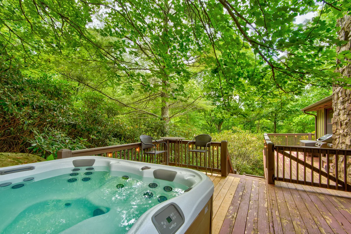 An inviting deck with a hot tub overlooking abundant surrounding greenery, offering a peaceful place for guests to unwind and enjoy the outdoors. The deck is integrated seamlessly with the natural landscape.
