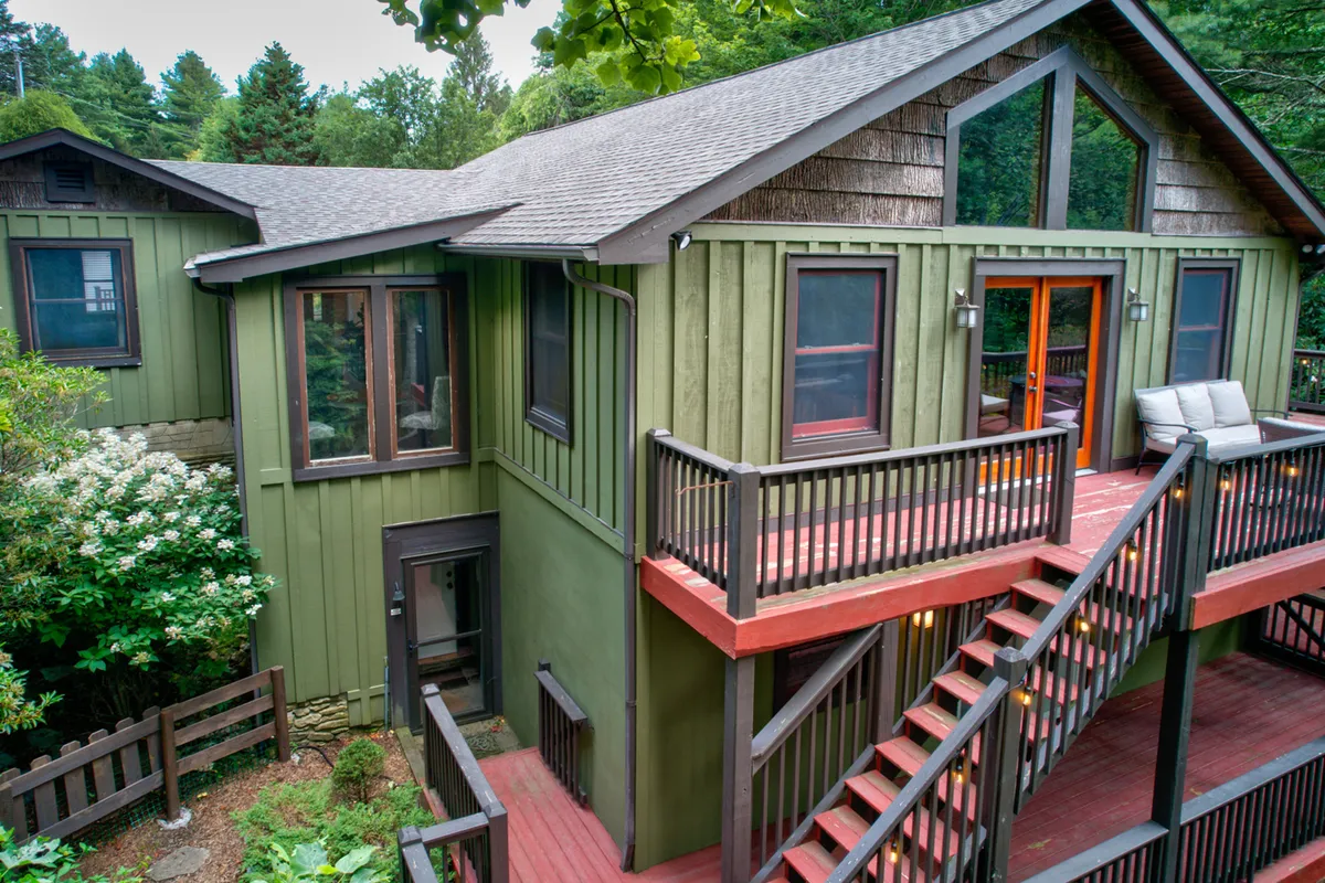 This image highlights the green exterior of Bigfoot Bungalow, showcasing its wooden balcony and railings, as well as an inviting outdoor seating area. The house is nestled amidst lush greenery, suggesting immediate access to nature and the tranquil setting that surrounds the property.