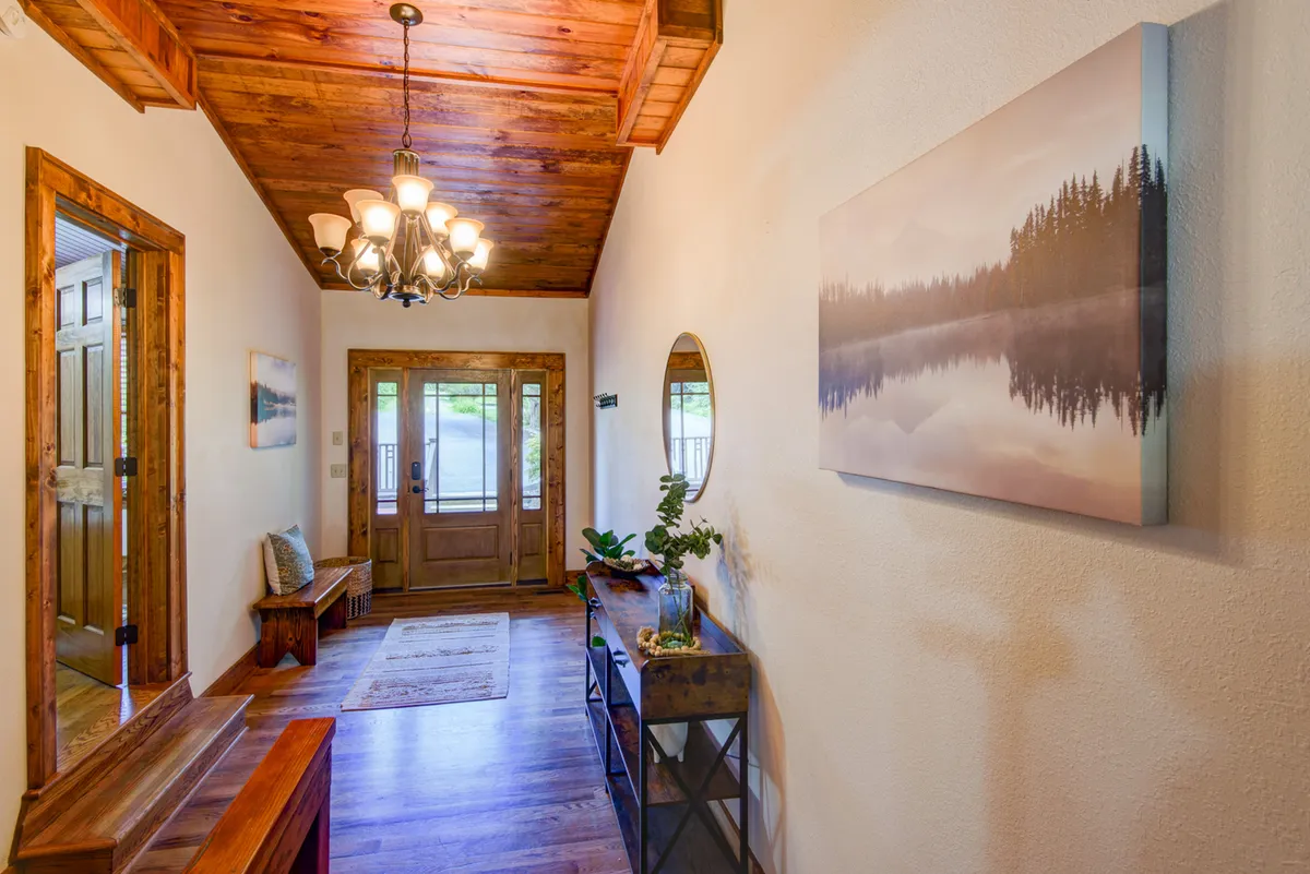 An interior shot focused on the entryway, featuring a cozy bench, a chandelier, a wooden door, and a mirror. The space is tidy and thoughtfully arranged, setting a warm and welcoming tone for guests as they step inside.