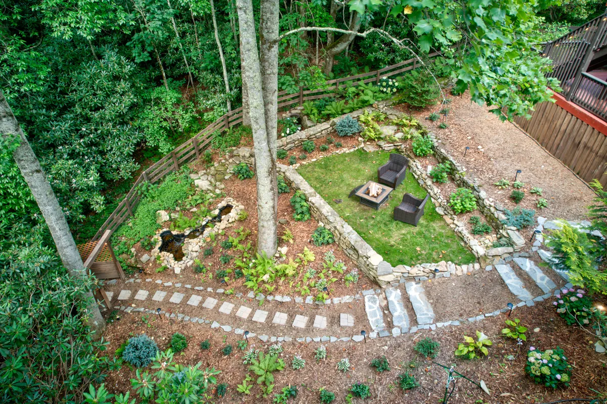An inviting stone fire pit area is set amidst a peaceful outdoor space, complete with comfortable seating and a meandering path. The natural landscaping and subtle water feature enhance the serene ambiance, providing the perfect venue for evening gatherings, storytelling, and s’mores around the fire.