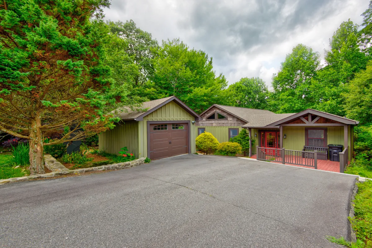 An inviting exterior shot featuring the front porch of the home, the green garage, and a well-maintained garden. The porch offers a welcoming space to relax while being surrounded by nature, hinting at the home’s accessibility and charm.
