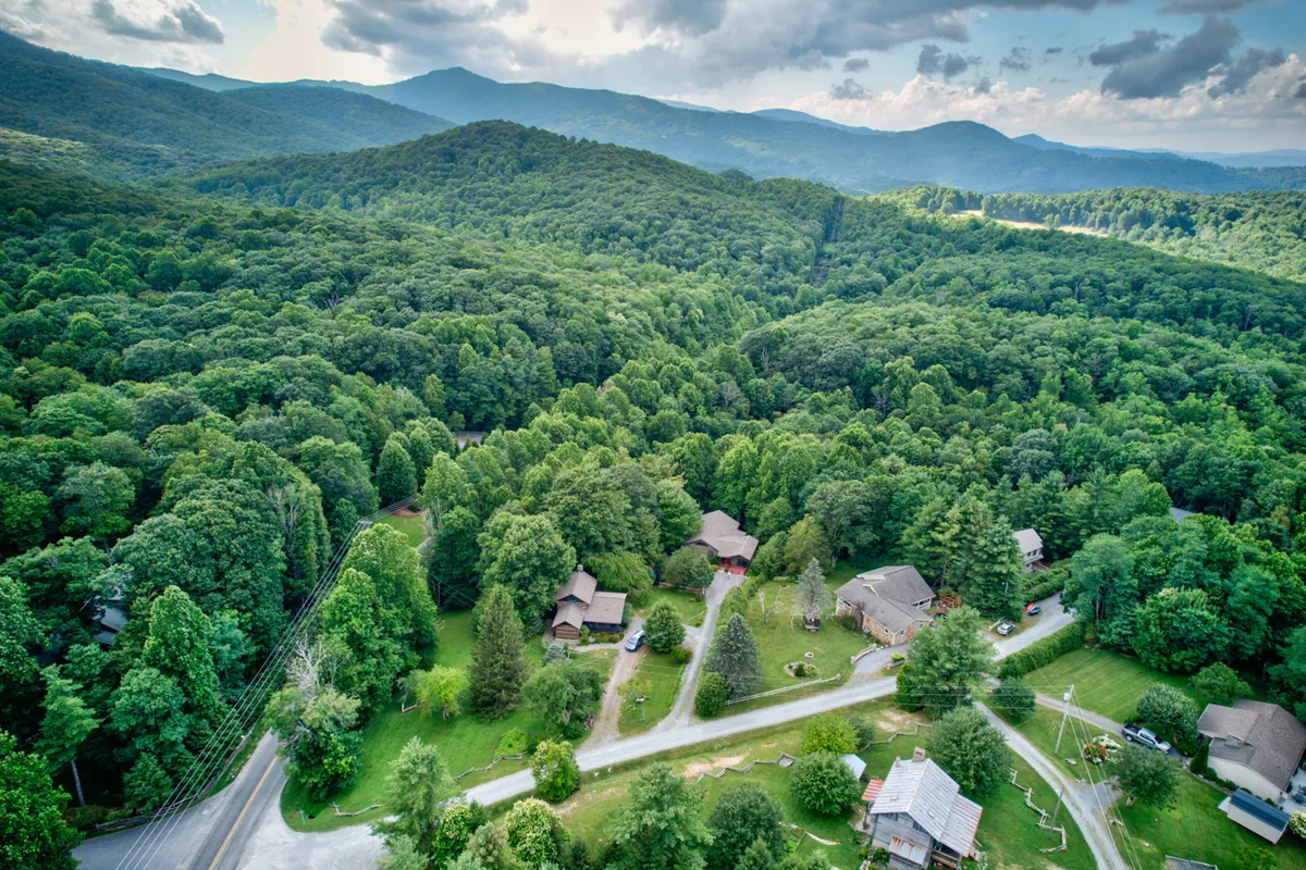 This exterior image captures rolling hills, wooded areas, scattered cabins, and winding roads, offering a wide view of the scenic Blue Ridge region. The natural landscape reflects opportunities for hiking, nature walks, and scenic drives near the home.