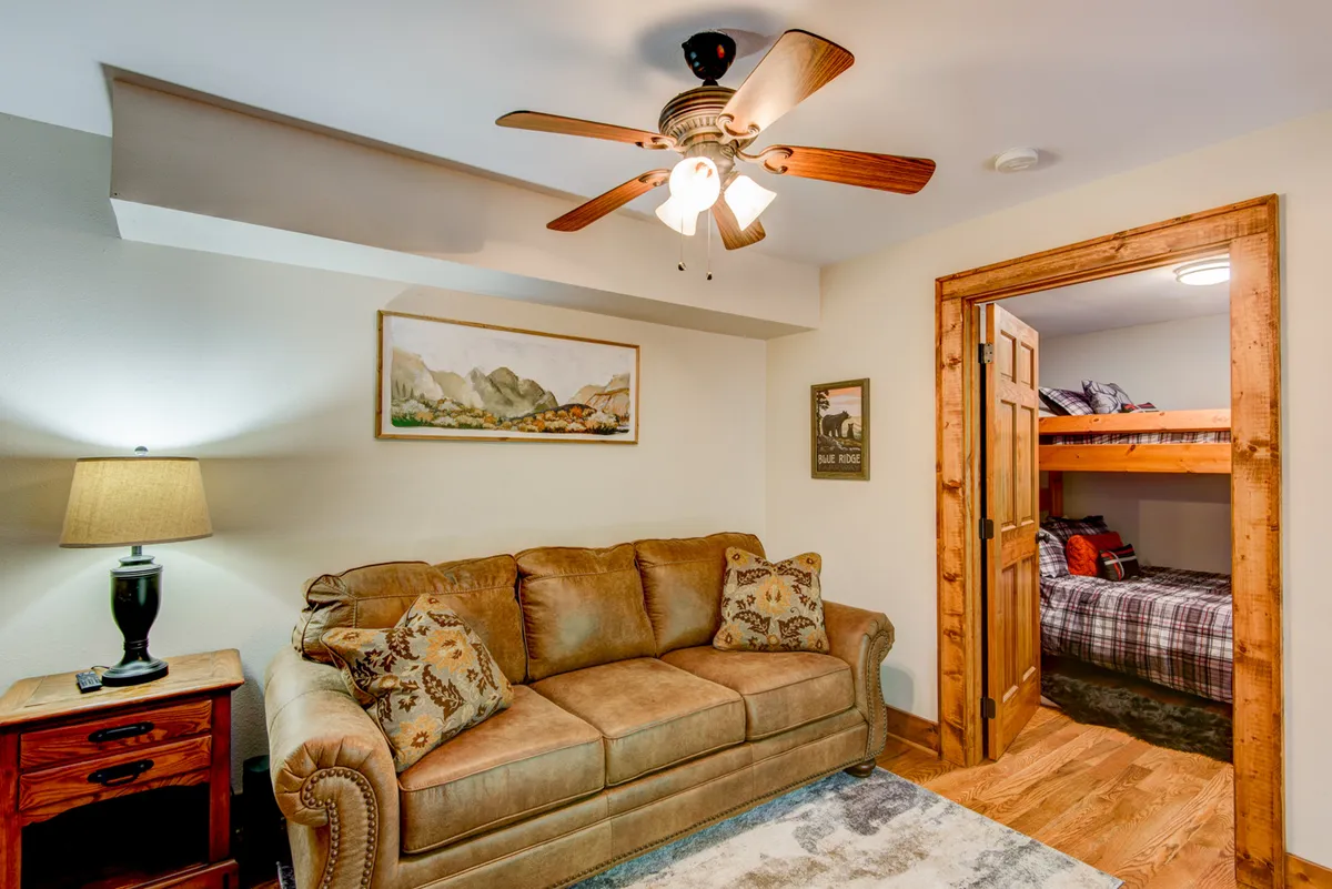 A kid-friendly bonus room featuring a cheerful sofa, bunk beds, soft lighting from a lamp, and playful wall art. The space is designed for relaxation, reading, playing games, or enjoying movie nights—perfect for children or extra friends.