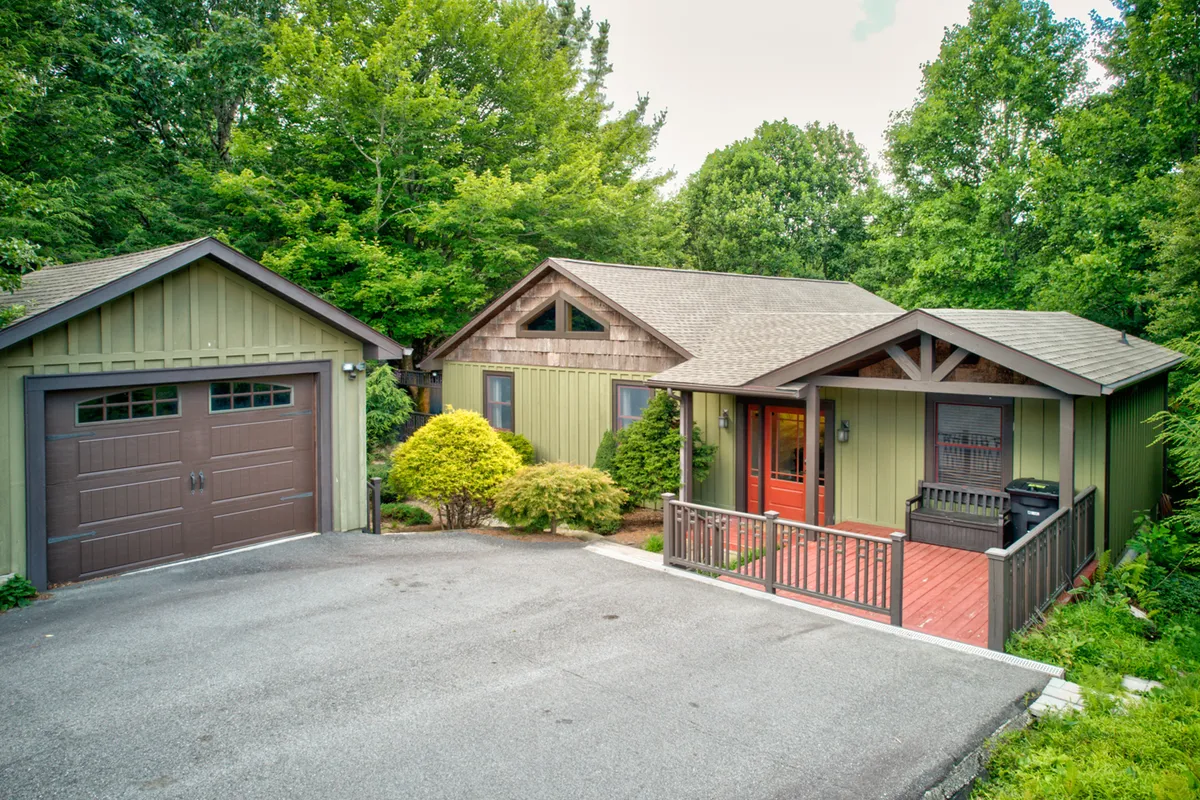 This exterior image presents the main entrance of the home, punctuated by a welcoming red door and a paved driveway leading directly to the covered porch. There is landscaped greenery around the entry, offering a cozy and inviting first impression. The garage is visible, adding to the sense of a well-maintained, secure property.
